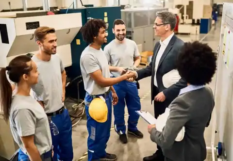 Apprentices in a manufacturing workshop shaking hands with a supervisor.