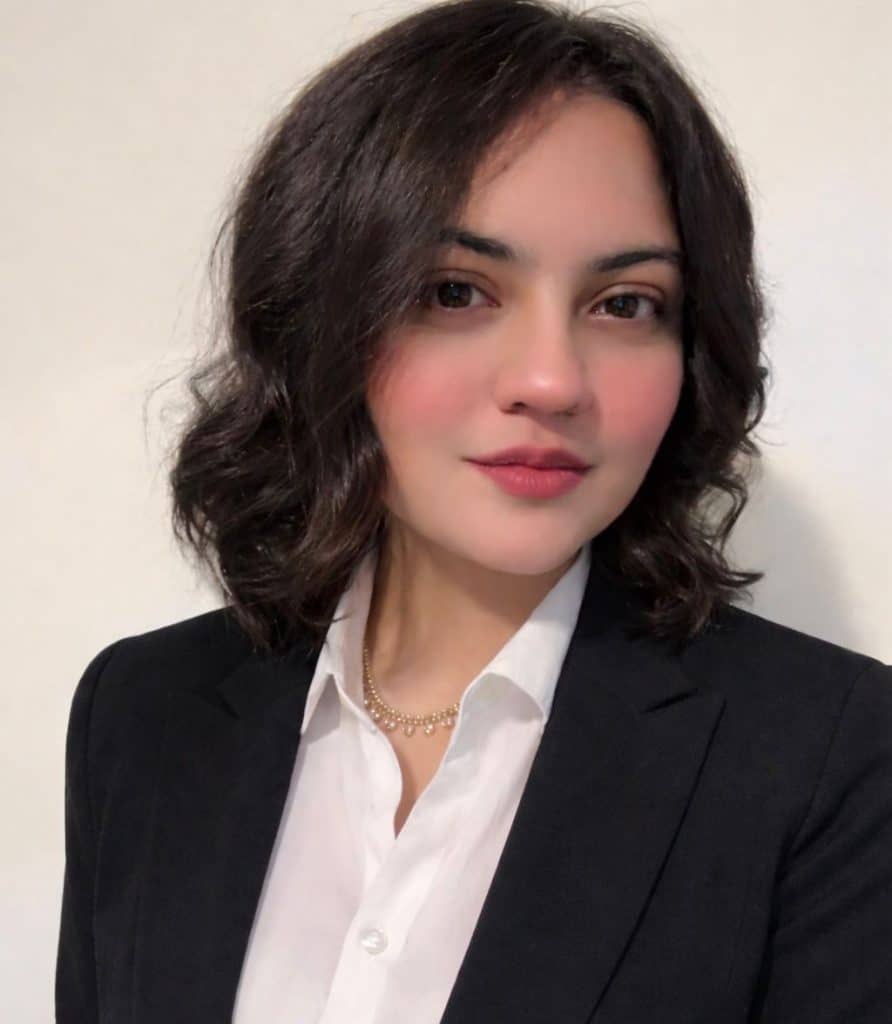 Professional woman in a black blazer and white shirt with wavy dark hair.