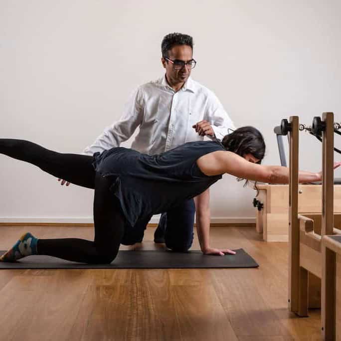 Enhanced yoga therapy session with instructor assisting a woman in a plank pose on a yoga mat.
