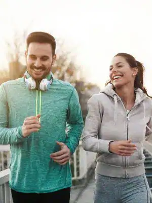 A smiling man and woman jogging outdoors in casual sportswear, enjoying exercise.