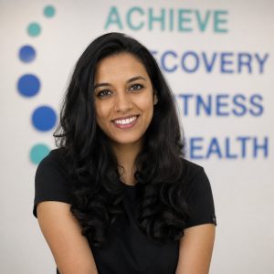 Smiling woman with long black hair in front of Therapia health and wellness background.